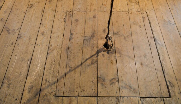 Old wooden floorboards with a rope pulling up a loose floor hatch.