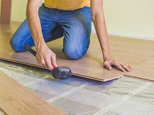 Worker fitting laminate floor panels over green underlayment floor